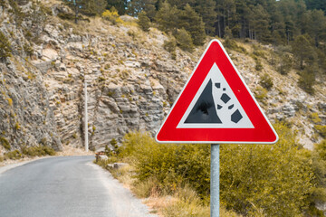 a large plaza triangular traffic sign informing about a dangerous section of the road with the fall of stones on mountain roads,