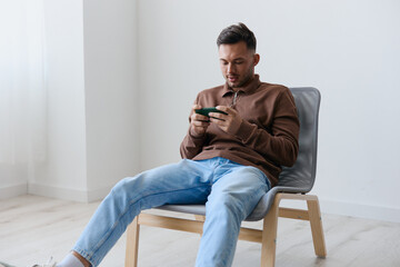 Mobile App concept. Concentrated focused confused attractive try to win playing in exciting raising game opening mouth looks at screen. Happy guy relaxing with phone chatting with friends. Copy space