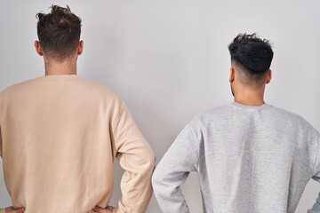 Young homosexual couple standing over white background standing backwards looking away with arms on...