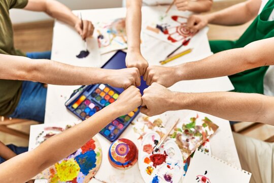 Group of people sitting on the table bump fists at art studio.