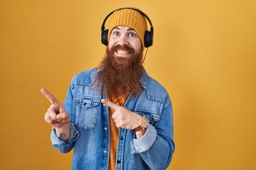 Caucasian man with long beard listening to music using headphones pointing aside worried and...