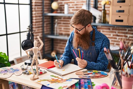 Young redhead man artist drawing on notebook at art studio