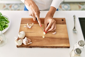 Young blonde woman cutting garlic at kitchen