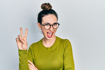 Young hispanic girl wearing casual clothes and glasses smiling with happy face winking at the camera doing victory sign. number two.