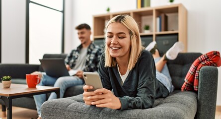 Young caucasian couple smiling happy using laptop and smartphone sitting on the sofa at home.