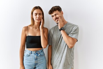 Naklejka premium Young beautiful couple standing together over isolated background touching mouth with hand with painful expression because of toothache or dental illness on teeth. dentist