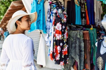 Naklejka premium Young hispanic woman wearing summer hat shopping at street market