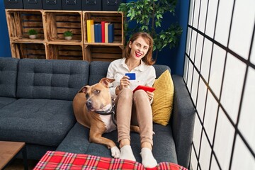 Young caucasian woman using touchpad and credit card sitting on sofa with dog at home