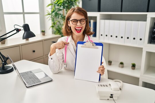 Young doctor woman wearing stethoscope holding clipboard pointing finger to one self smiling happy and proud