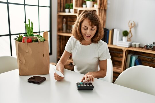 Young caucasian woman smiling confident doing accounting of groceries purchase at home