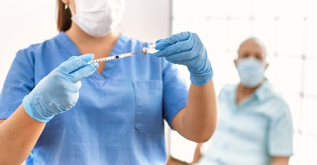 Young nurse wearing safety mask preparing coronavirus vaccine to vaccinate senior man