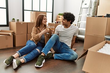 Young couple smiling happy toasting with glass of wine at new home.