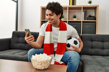 Young hispanic man watching soccer match and supporting team at home.