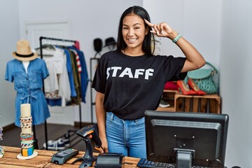 Young hispanic woman working as staff at retail boutique smiling pointing to head with one finger, great idea or thought, good memory