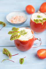 Tomato juice with sorrel, salt and sour cream in glass on blue wooden background. Side view, selective focus.