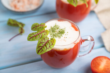 Tomato juice with sorrel, salt and sour cream in glass on blue wooden background. Side view, selective focus.