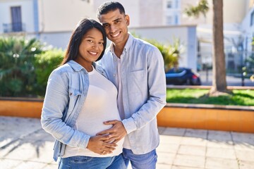 Young latin couple expecting baby hugging each other standing at park