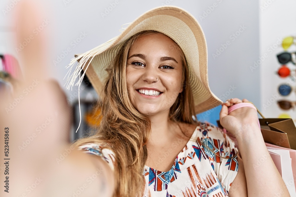 Wall mural Young blonde girl wearing hat make selfie by the camera at clothing store