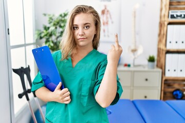 Young caucasian woman working at pain recovery clinic showing middle finger, impolite and rude fuck...
