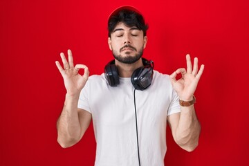 Hispanic man with beard wearing gamer hat and headphones relaxed and smiling with eyes closed doing meditation gesture with fingers. yoga concept.