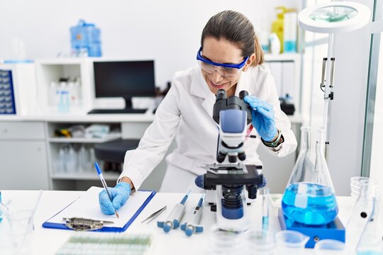 Young hispanic woman wearing scientist uniform using microscope at laboratory