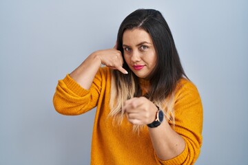 Young hispanic woman standing over isolated background smiling doing talking on the telephone...
