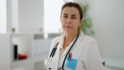 Middle age hispanic woman wearing doctor uniform standing with relaxed expression at clinic