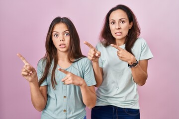 Young mother and daughter standing over pink background pointing aside worried and nervous with...
