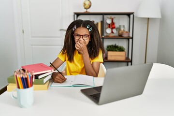 Young african american girl doing homework at home smelling something stinky and disgusting,...