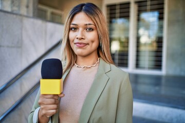 Young latin woman smiling confident using microphone at street