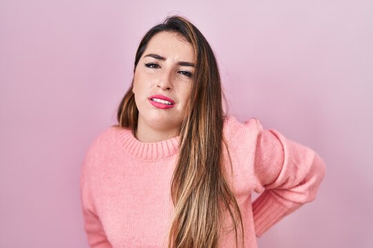 Young hispanic woman standing over pink background suffering of backache, touching back with hand, muscular pain