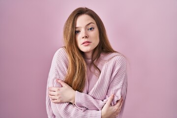 Obraz premium Young caucasian woman standing over pink background shaking and freezing for winter cold with sad and shock expression on face