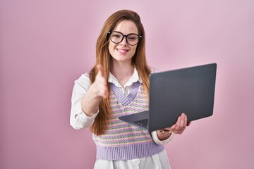 Young caucasian woman working using computer laptop smiling friendly offering handshake as greeting and welcoming. successful business.