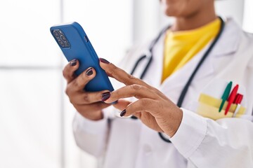 African american woman wearing doctor uniform using smartphone at clinic
