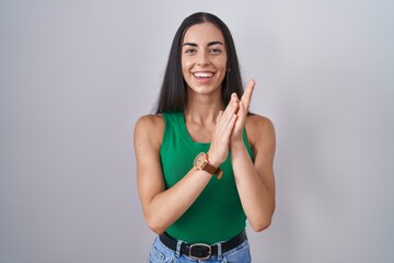 Young woman standing over isolated background clapping and applauding happy and joyful, smiling...