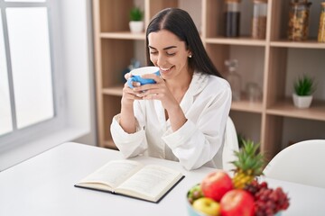 Young hispanic woman reading book drinking coffee at home