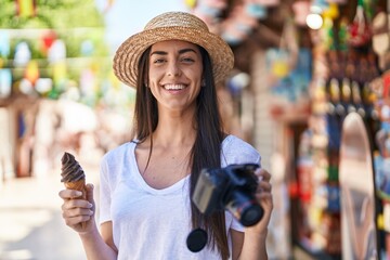 Young hispanic woman tourist eating ice cream holding reflex camera at street market