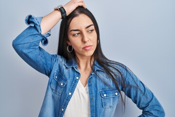 Hispanic woman standing over blue background confuse and wondering about question. uncertain with...