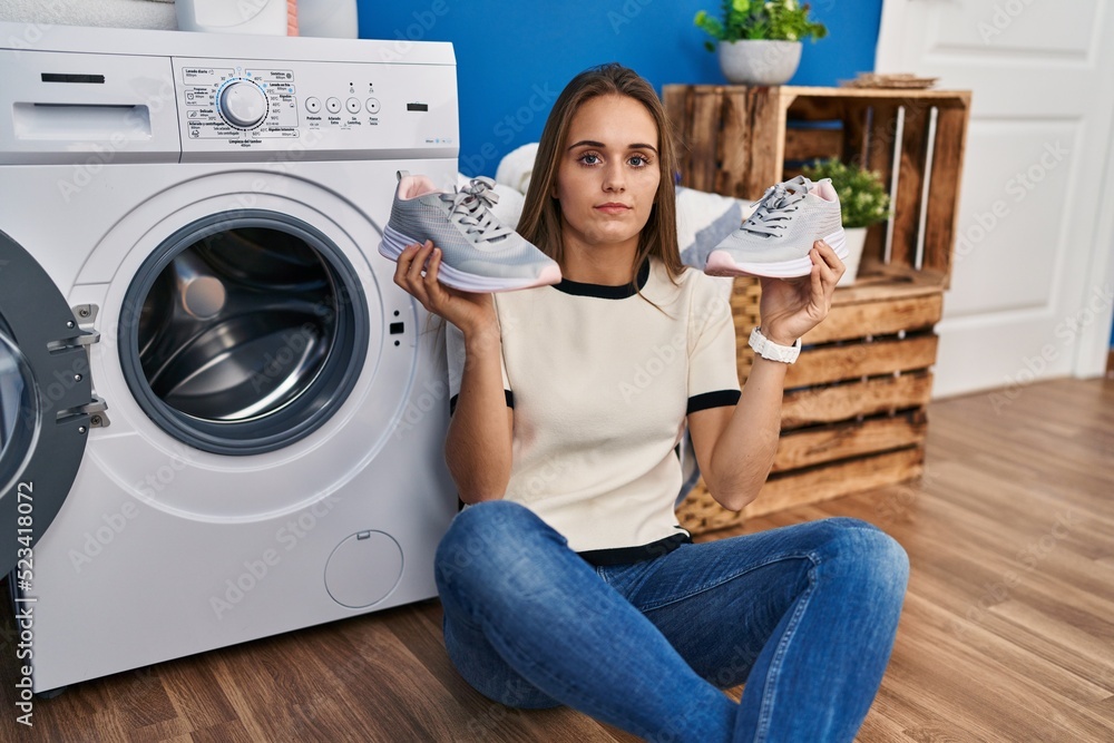 Poster young woman putting sneakers in washing machine relaxed with serious expression on face. simple and 