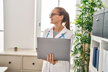 Young blonde woman wearing doctor uniform using laptop working at clinic