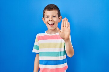 Young caucasian kid standing over blue background waiving saying hello happy and smiling, friendly welcome gesture