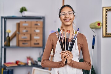 Young african american woman artist smiling confident holding paintbrushes at art studio
