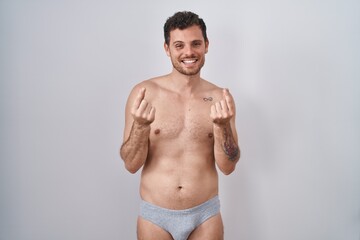 Fototapeta premium Young hispanic man standing shirtless wearing underware doing money gesture with hands, asking for salary payment, millionaire business