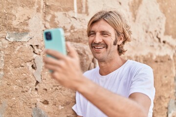 Fototapeta premium Young blond man smiling confident making selfie by the smartphone at street
