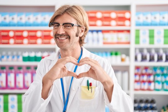 Caucasian man with mustache working at pharmacy drugstore smiling in love doing heart symbol shape with hands. romantic concept.