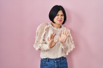 Young asian woman standing over pink background disgusted expression, displeased and fearful doing...