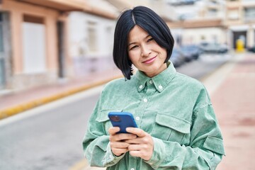 Fototapeta premium Young chinese woman smiling confident using smartphone at street