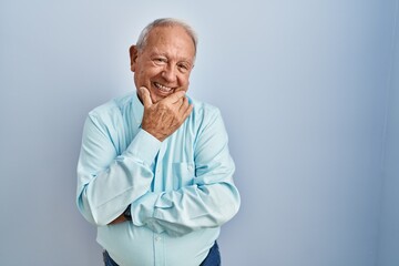 Senior man with grey hair standing over blue background looking confident at the camera smiling with crossed arms and hand raised on chin. thinking positive.