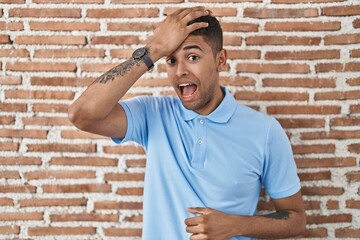 Brazilian young man standing over brick wall surprised with hand on head for mistake, remember...
