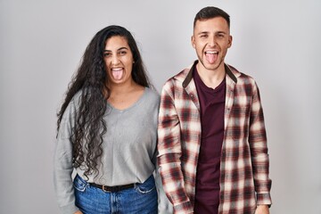 Young hispanic couple standing over white background sticking tongue out happy with funny expression. emotion concept.